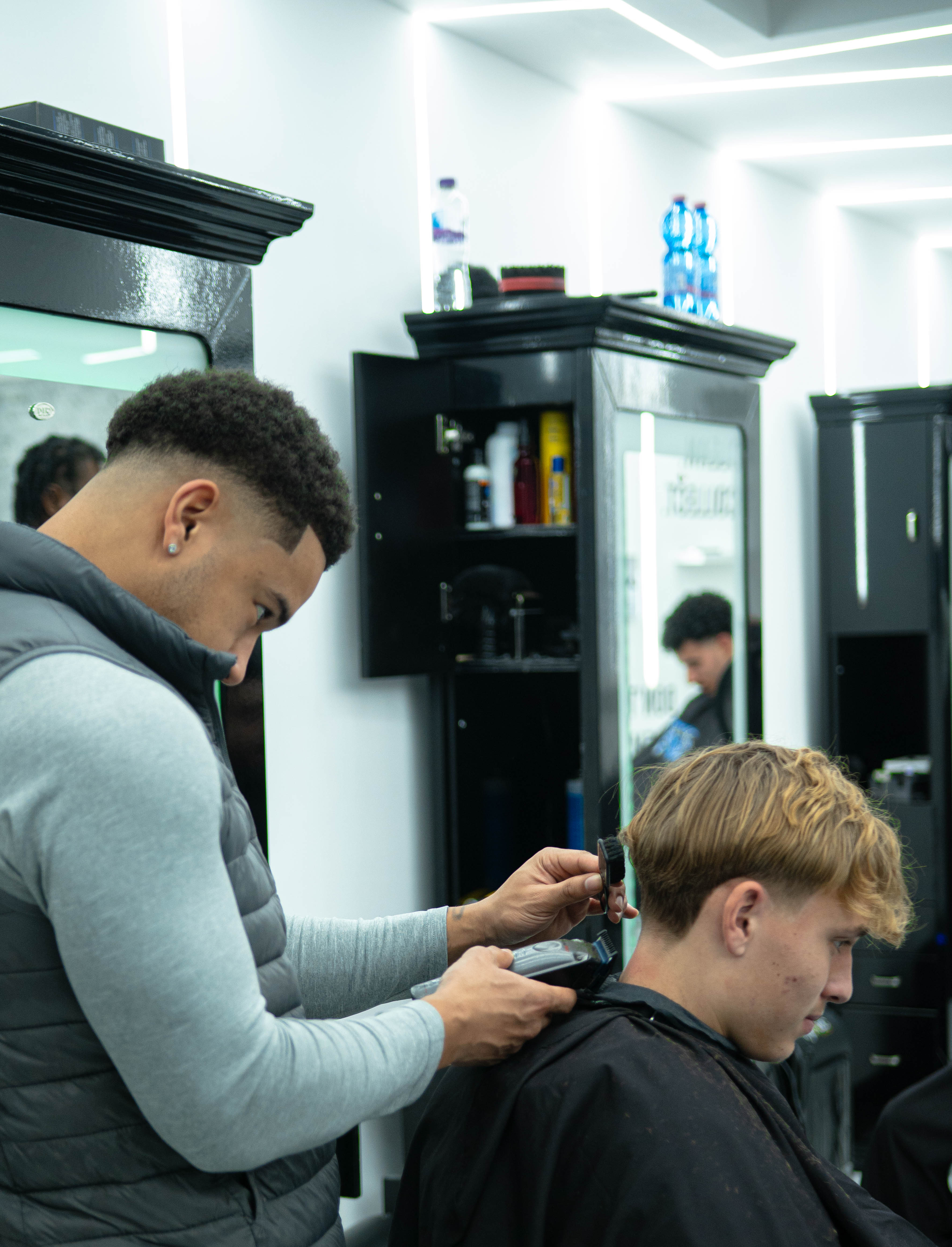 Barber trimming the hair on the back of a young man's head in a modern barbershop.