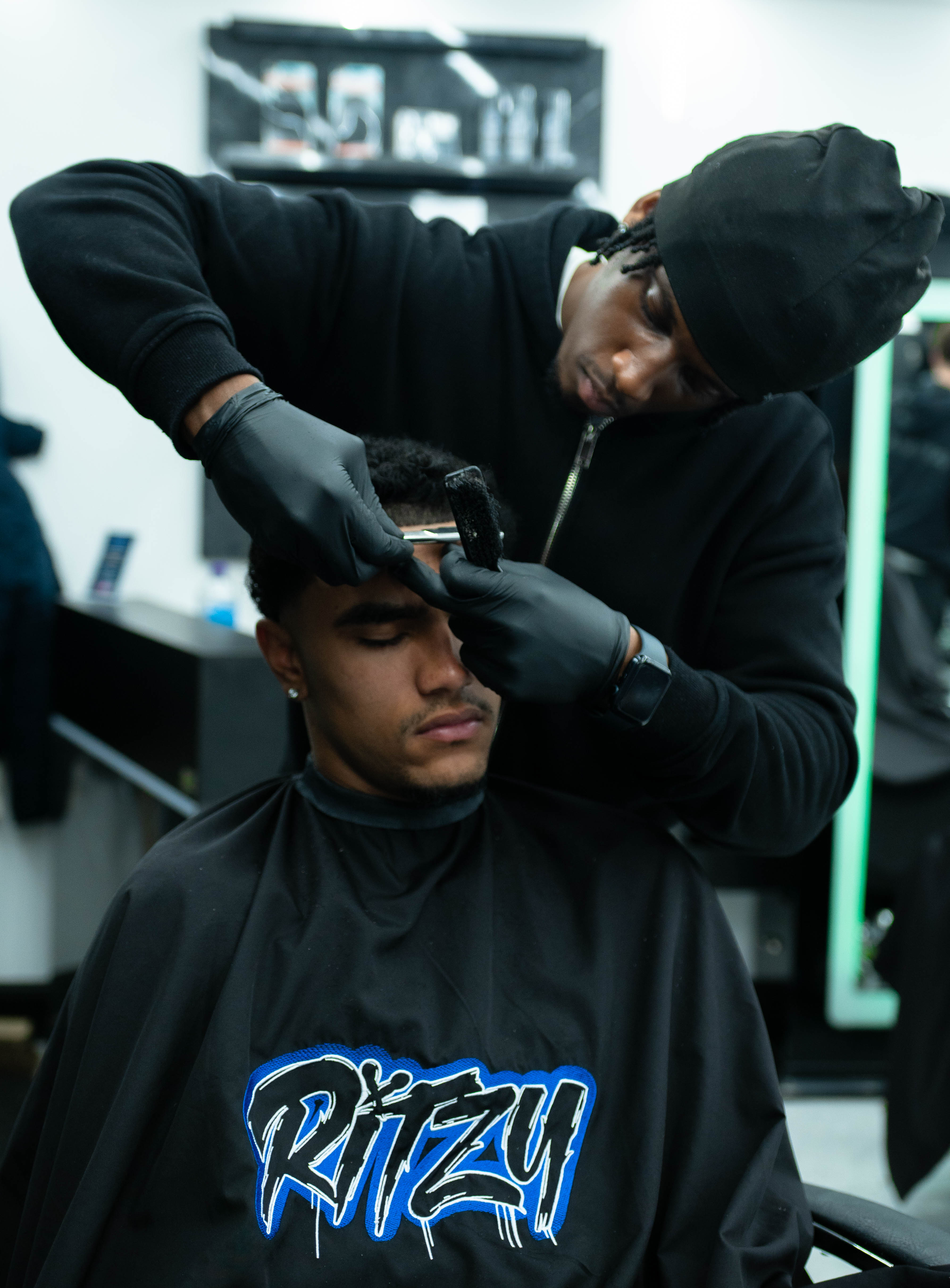 Barber wearing black gloves trimming a young man's hair at a barbershop.