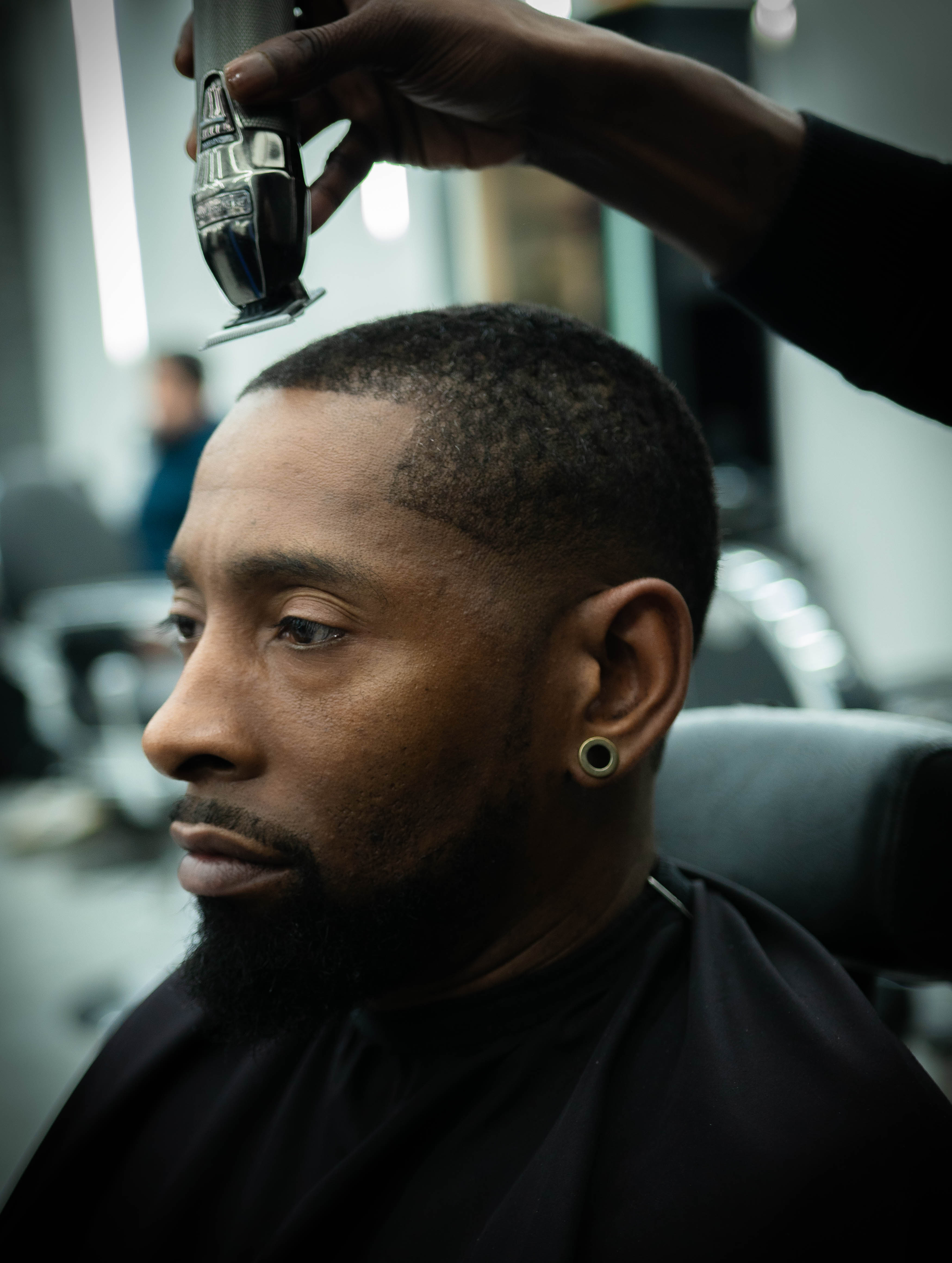 Man with a beard getting a close haircut with electric clippers in a barbershop.
