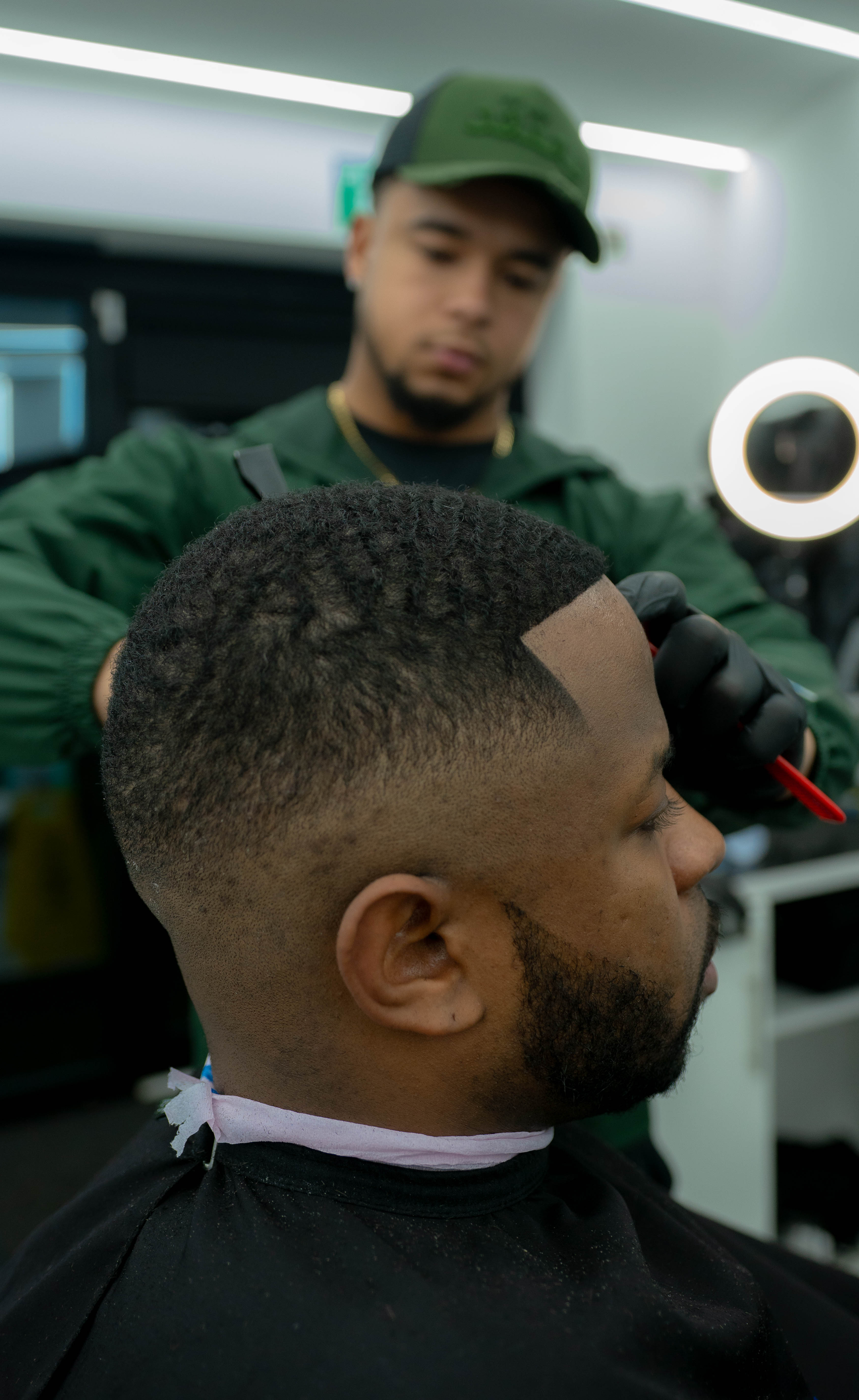 Barber shaping the hairline of a seated man with a fresh fade haircut in a barbershop.