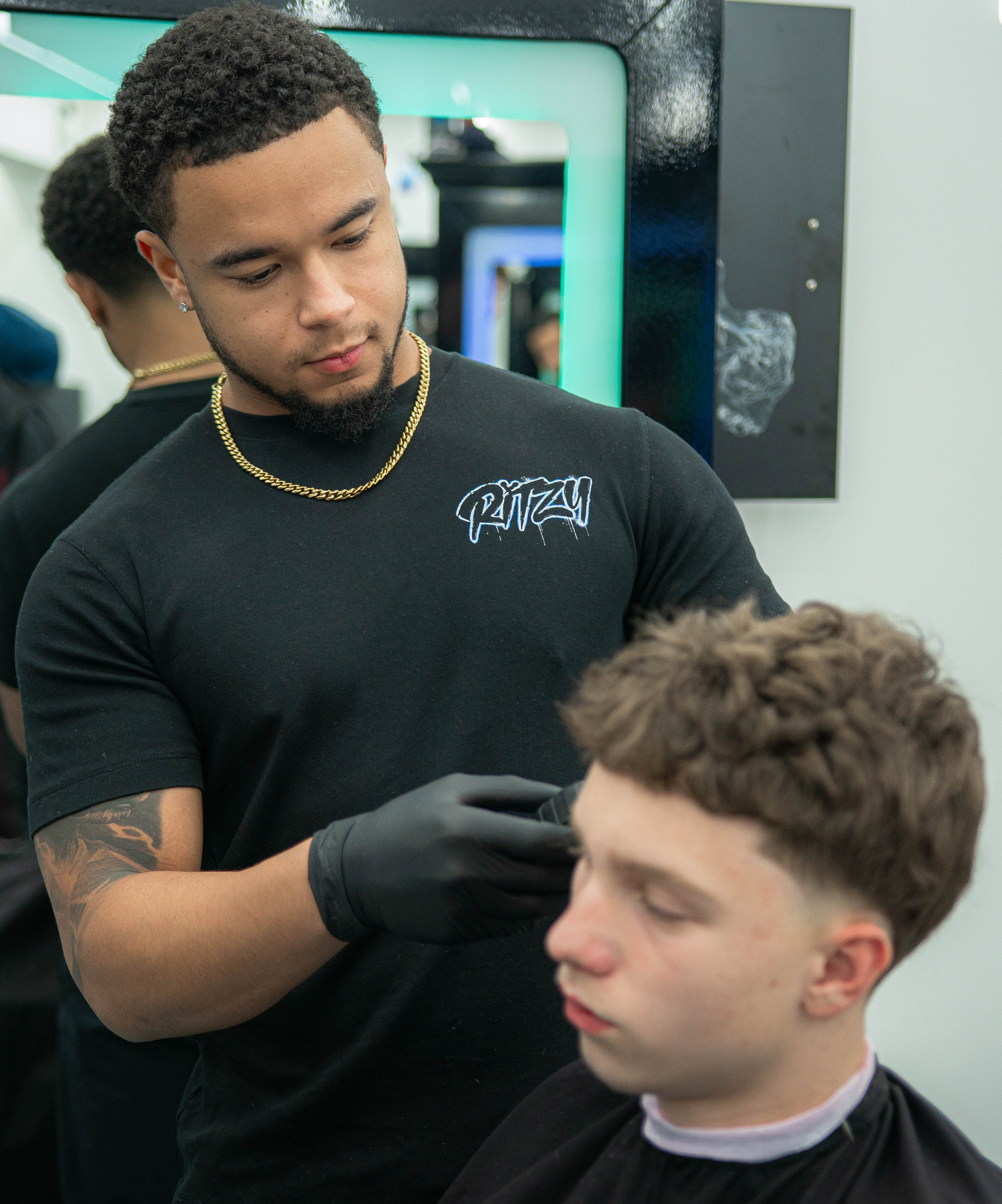 Barber wearing a black shirt and gloves giving a haircut to a young man in a salon in Peterborough 