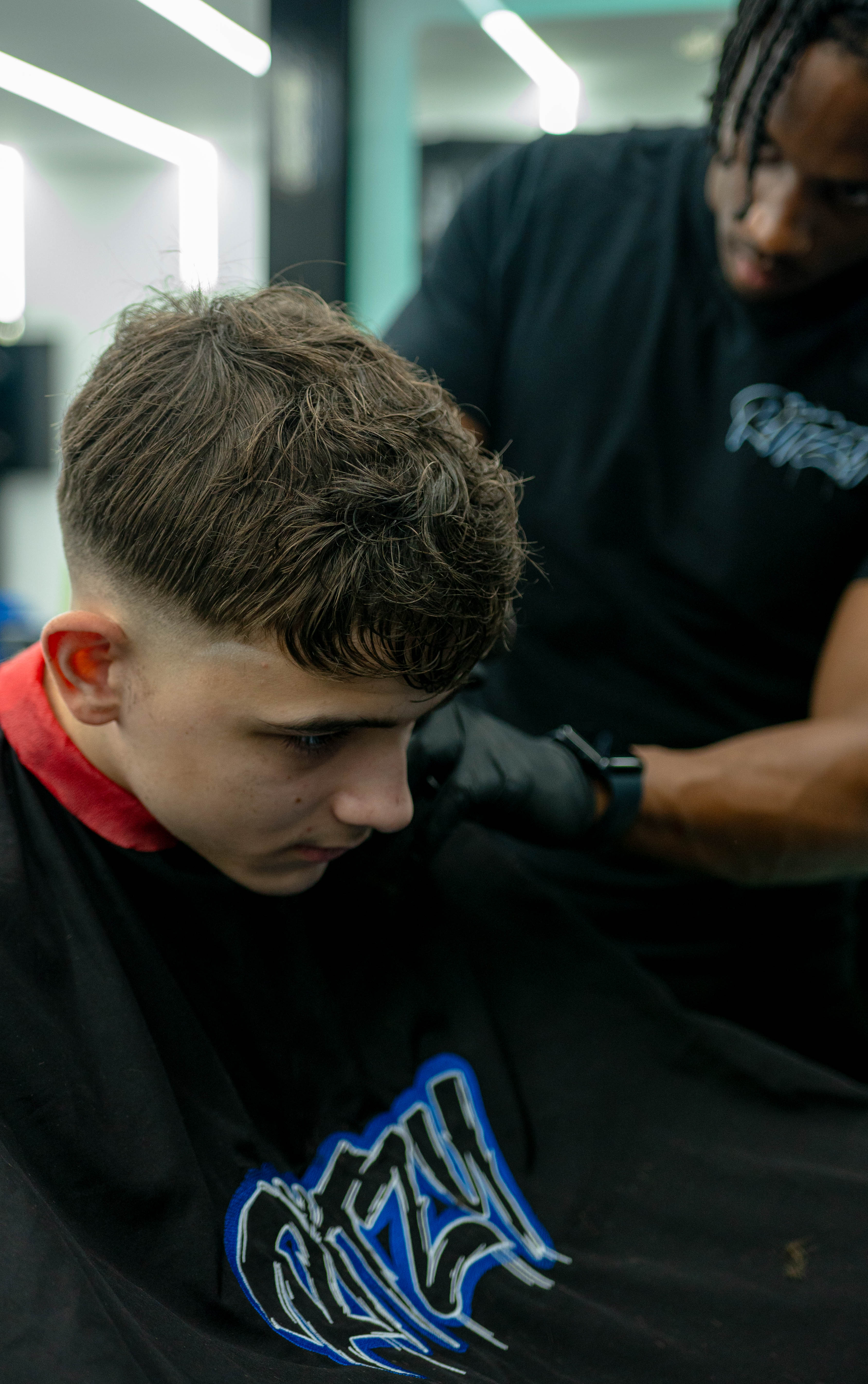 Young man with short brown hair getting a haircut from a barber wearing black gloves.