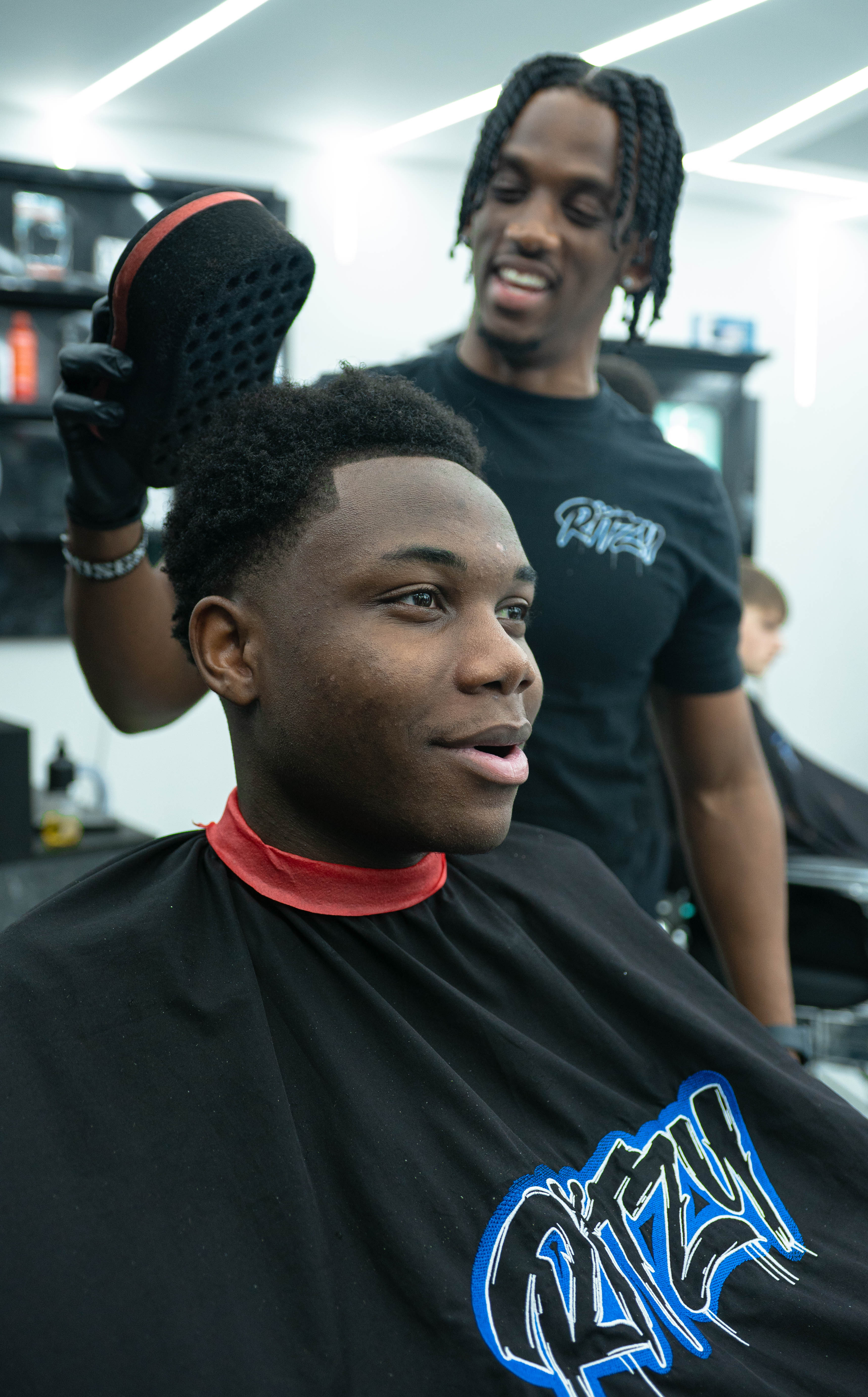 Barber holding a brush near a smiling man with a fresh haircut in a barbershop in Peterborough 
