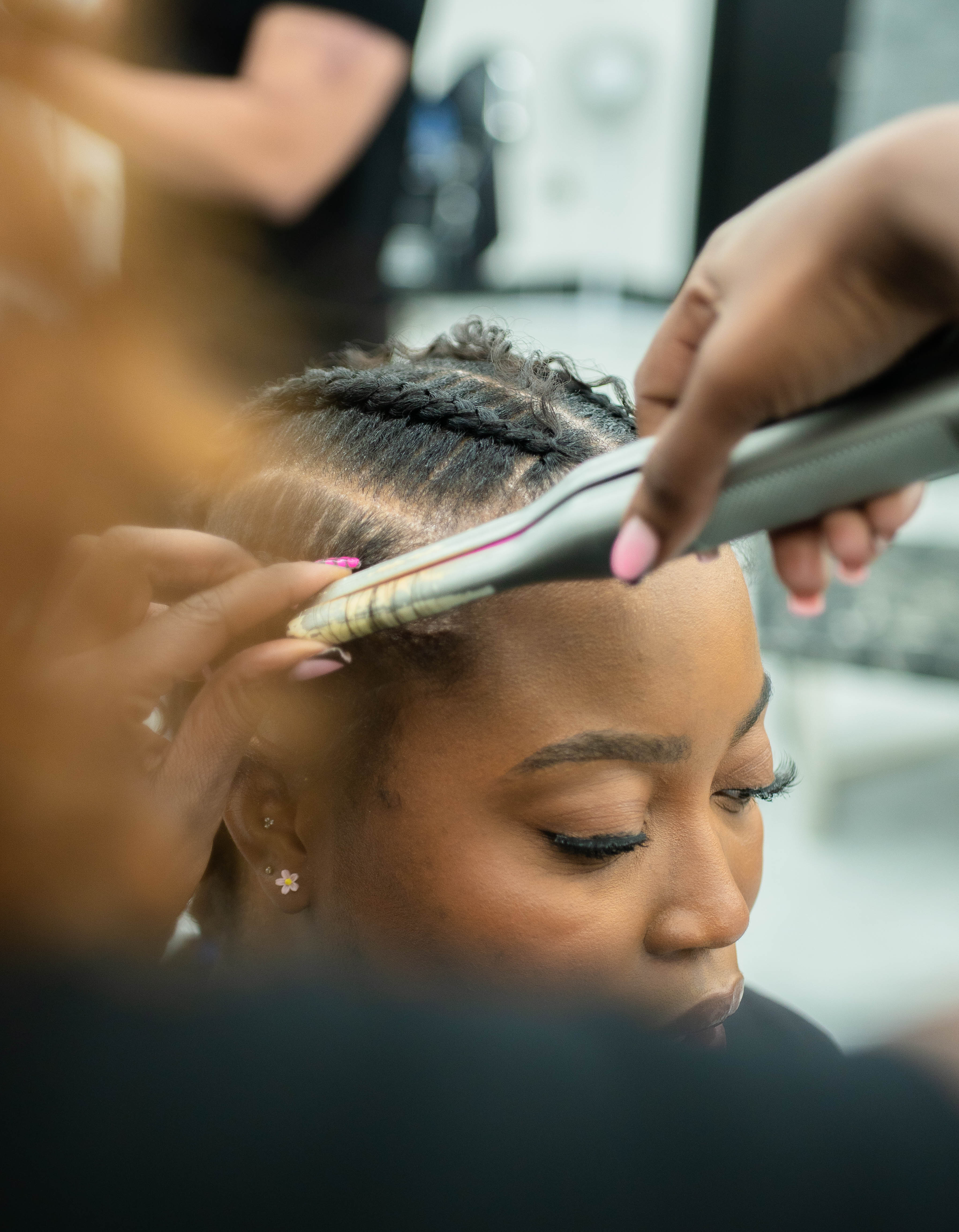 Close-up of a woman having her hair styled with a flat iron on braids near the hairline.