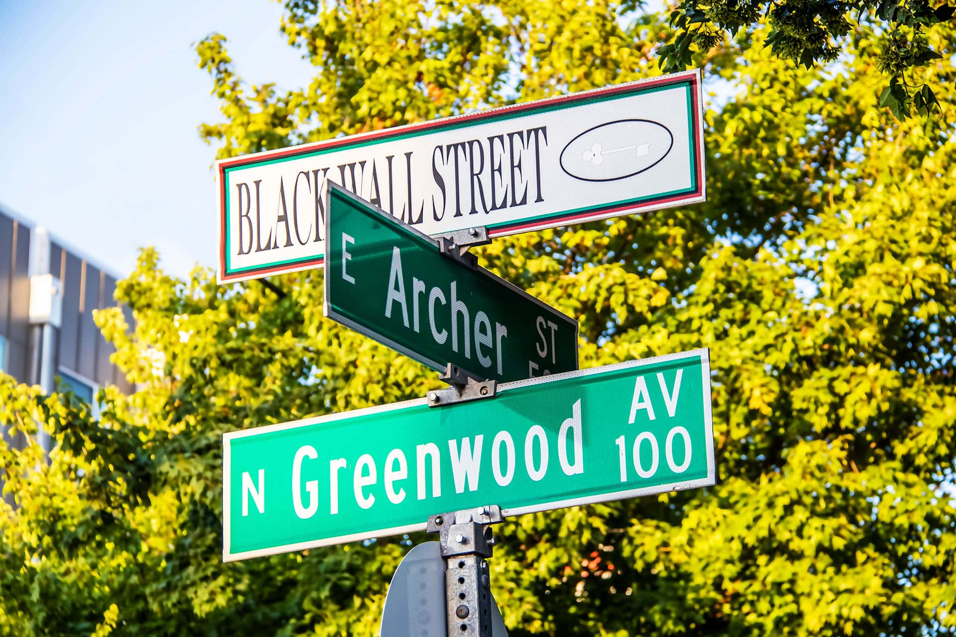 Street signs marking the intersection of E Archer St. and N Greenwood Ave. with a Black Wall Street street sign posted above them.