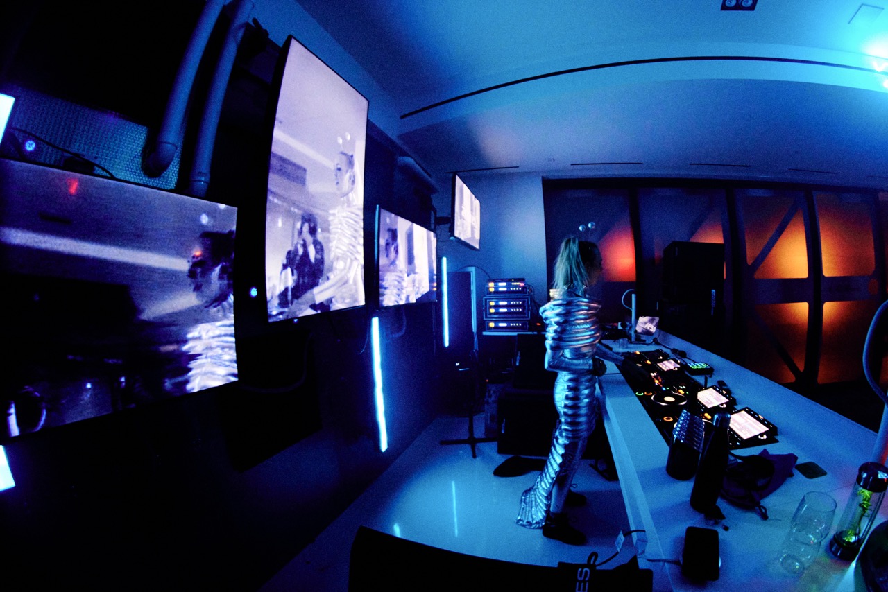 DJ booth with blue alien lighting, a backdrop wall featuring screens, pipes, and integrated lighting.