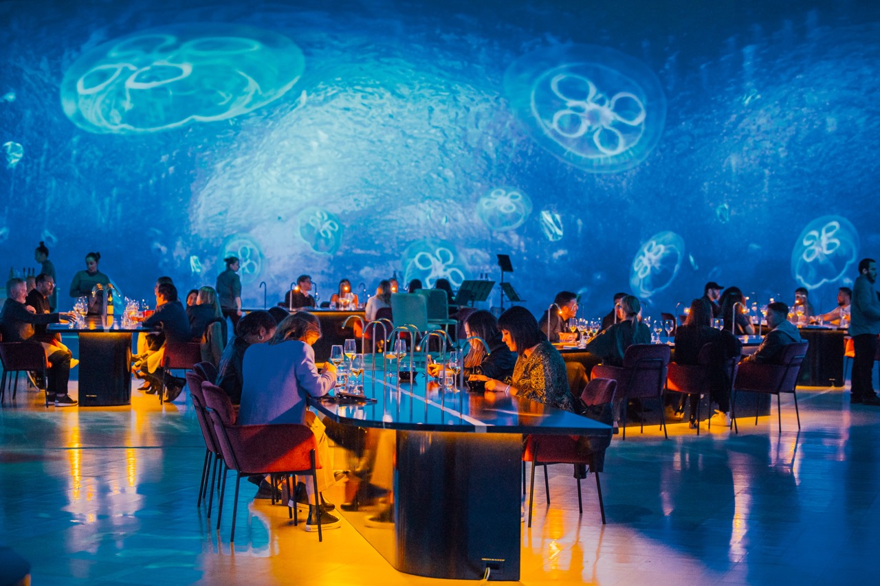 A luxury dining set up with custom marble tables, set within a virtual room currently displaying an underwater jellyfish scene. 