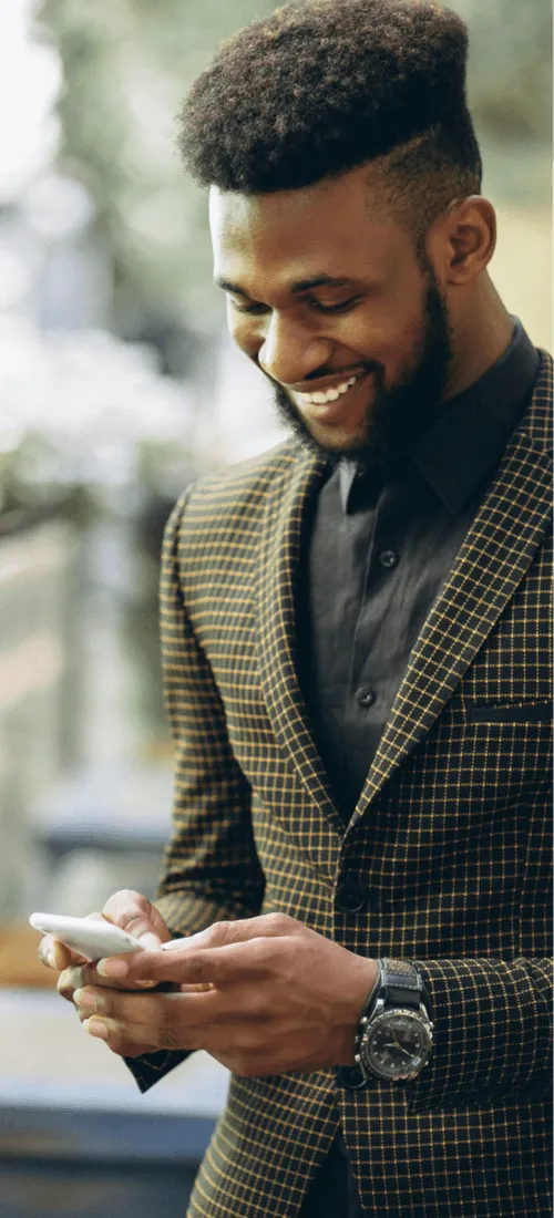 Smiling man in checkered blazer looking at his smartphone outdoors.