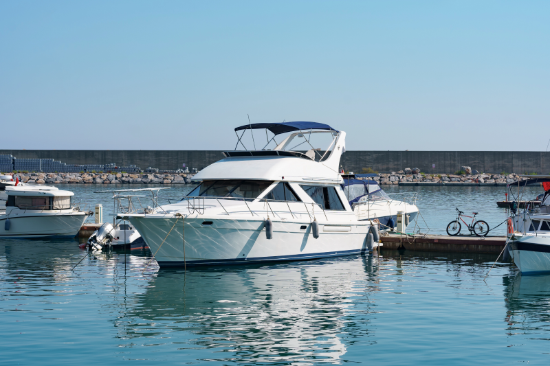 White motor yacht docked at a marina with calm blue water and clear sky.