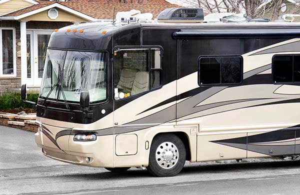 Side view of a beige and black motorhome parked on a residential street in front of a house.