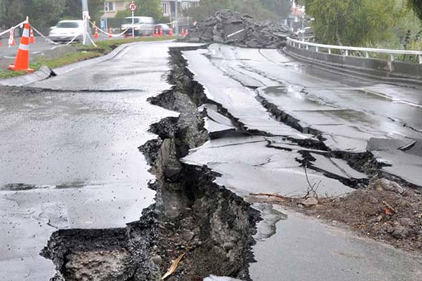 Severely cracked and buckled road with large fissures and debris, indicating earthquake damage.