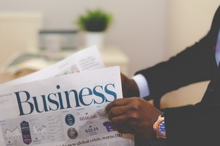 Close-up of a person reading a newspaper with the headline Business, wearing a suit and a wristwatch.