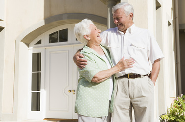 Elderly couple smiling and embracing outside a building with white doors and pillars.