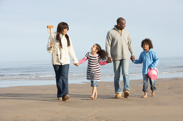 Family of four walking barefoot on a sandy beach with the ocean in the background.