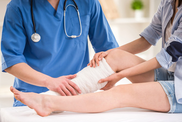 Medical professional in blue scrubs wrapping a patient's lower leg with a bandage.