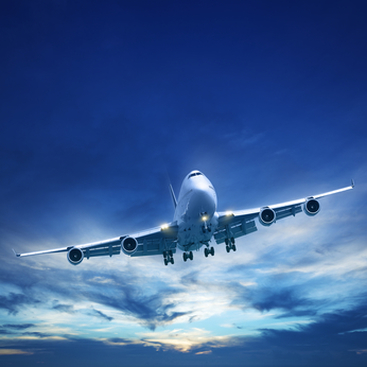 Large passenger airplane flying against a clear blue sky with scattered clouds at sunset.