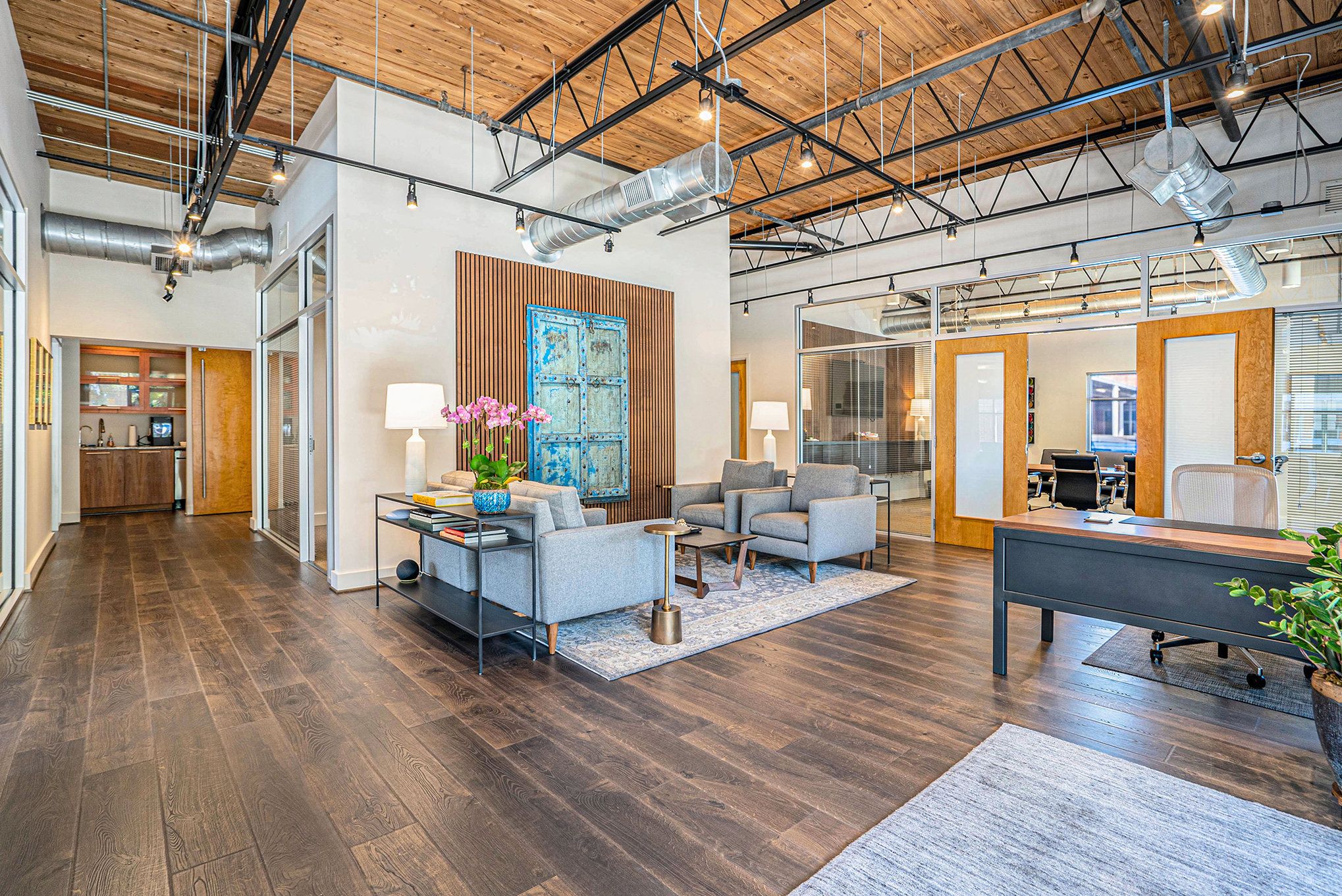 Blue Door Mediation interior: modern office lounge area with gray sofas and armchairs on a rug, a blue cabinet wall art, wooden floor, and exposed ceiling ducts.