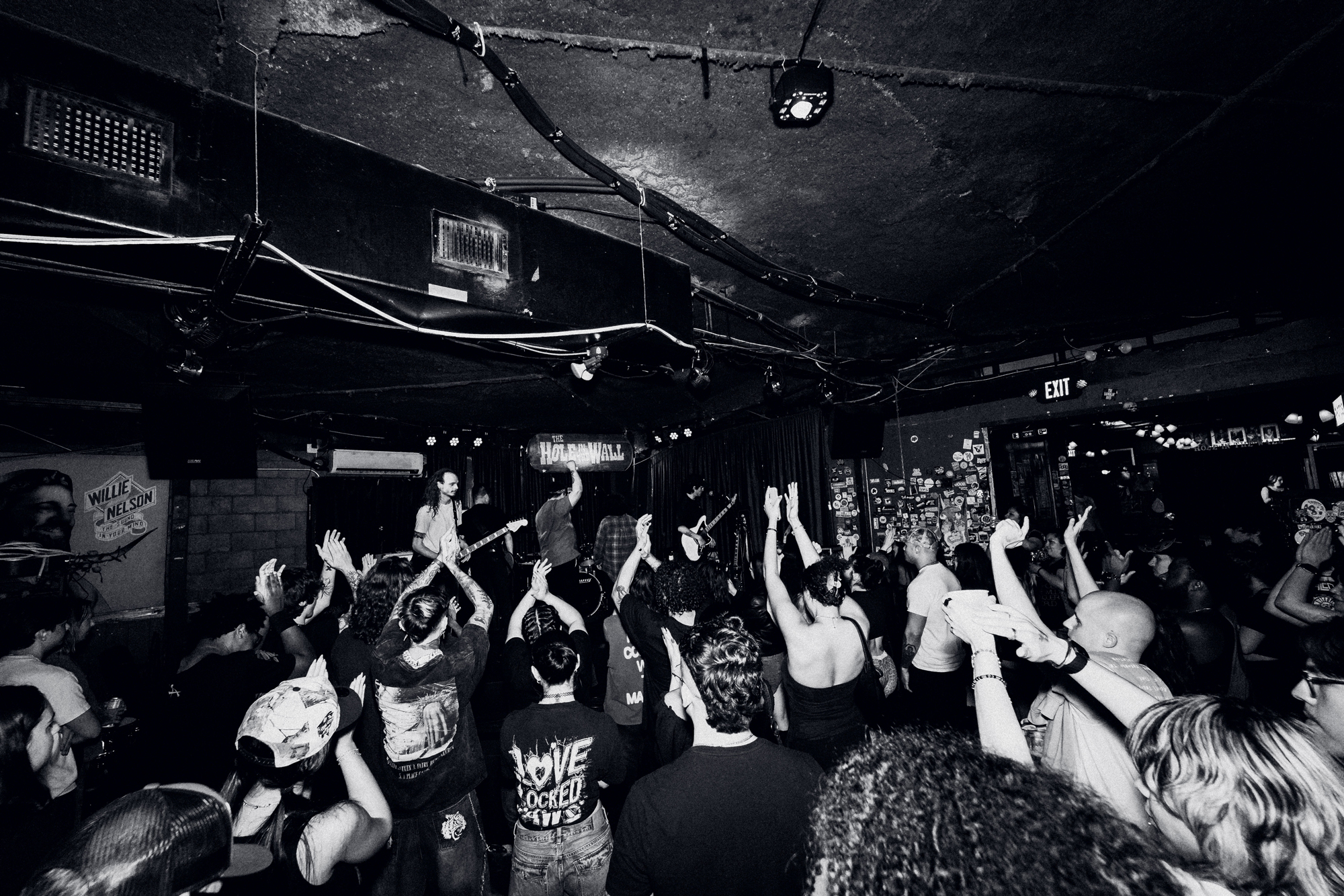 Crowd clapping and cheering at a live indoor concert with guitarists performing on stage.