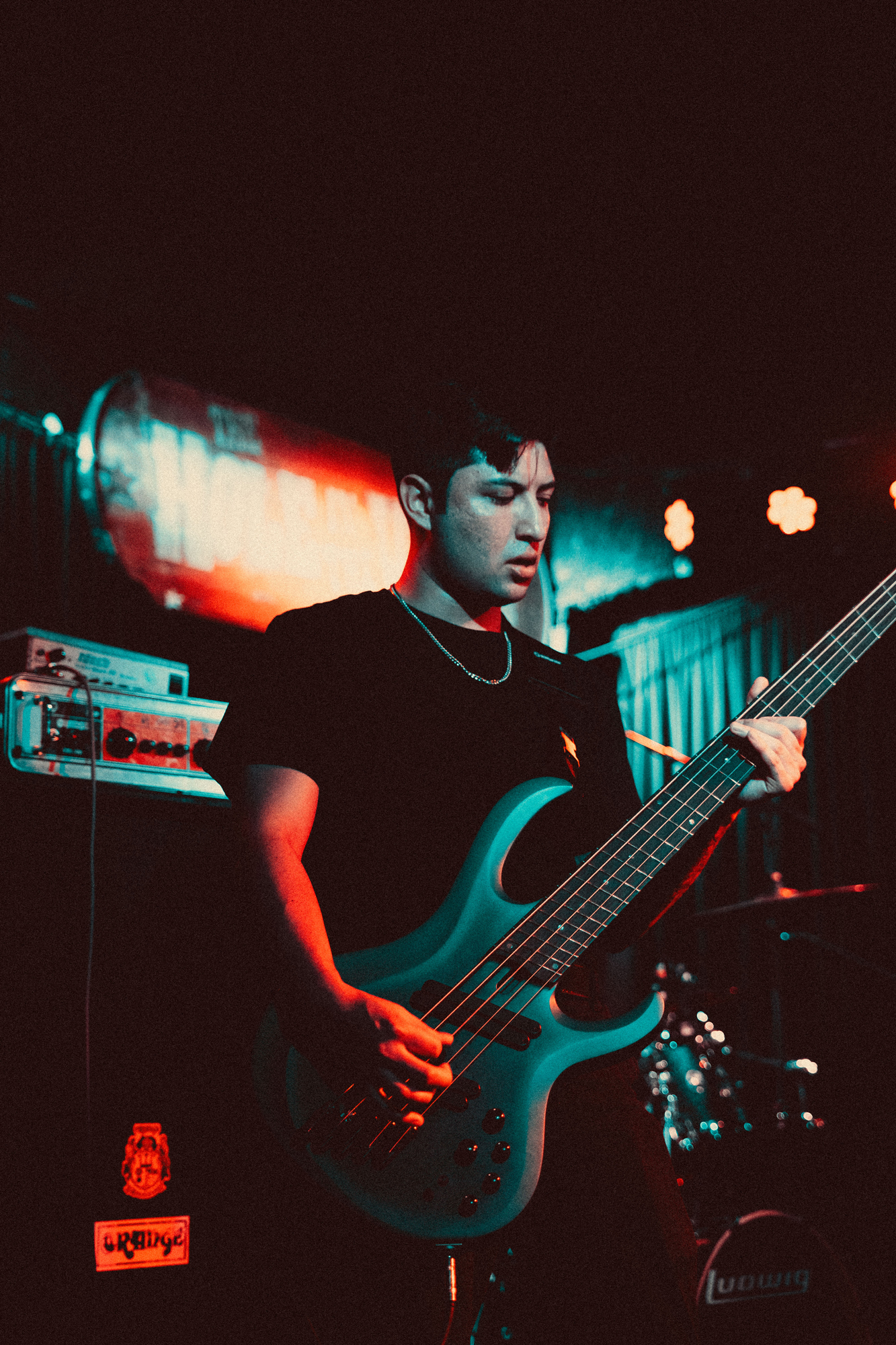 Man playing electric bass guitar on stage with blue and red lighting.