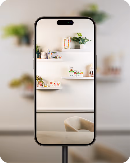 Smartphone on a stand showing a white wall with small floating shelves holding potted plants and decorative items in a cozy room.