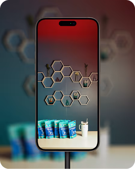 Smartphone displaying a shelf with hexagonal compartments holding small plants and bottles, with a row of blue-green product packages and a white cup with a straw on a table in front.