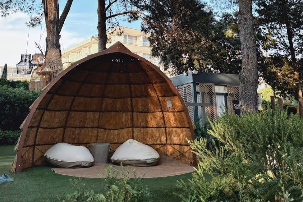 Outdoor shaded lounge with two cushioned seats under a wooden dome structure in a garden.