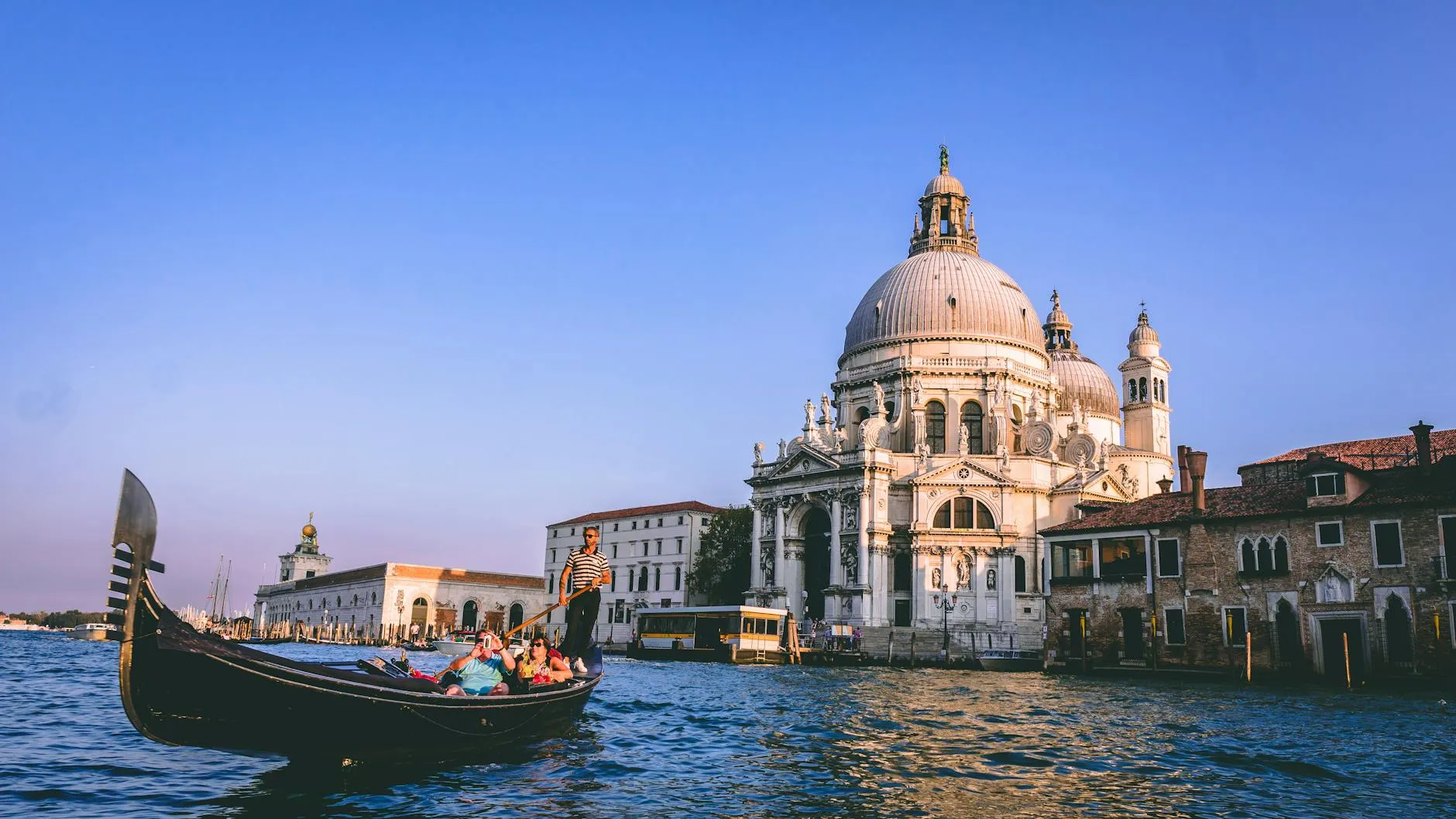 Gondola with passengers on water in front of a large domed historic building under a clear sky.