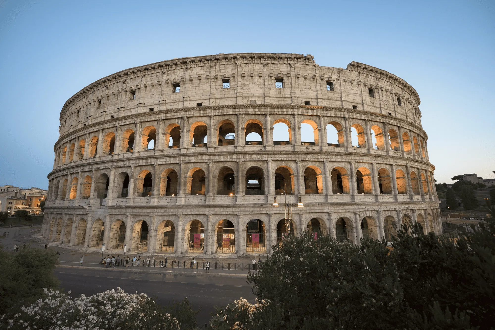 The Colosseum in Rome illuminated at dusk with a clear blue sky.