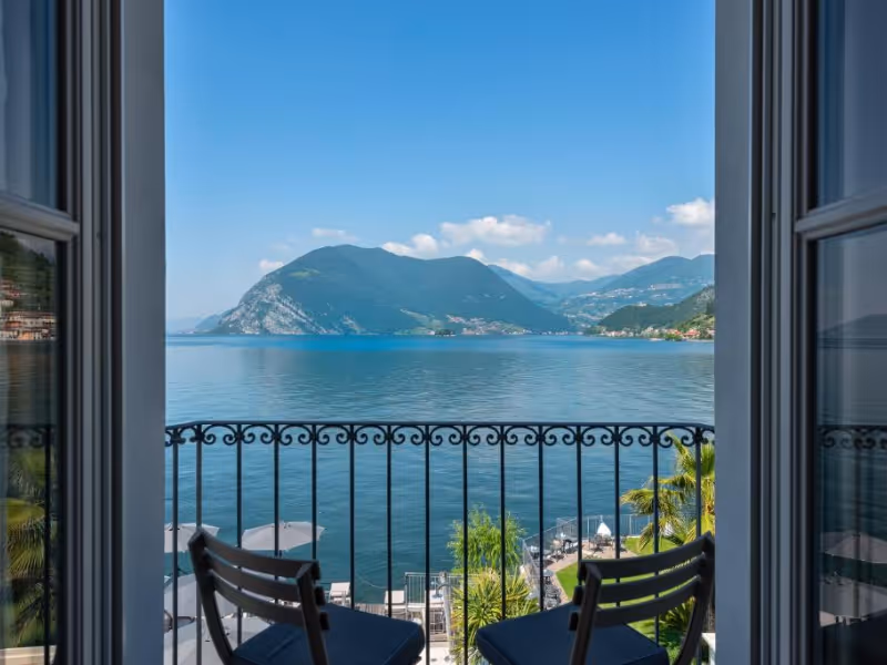 View of a calm lake and mountains from a balcony with two chairs and an ornate railing.