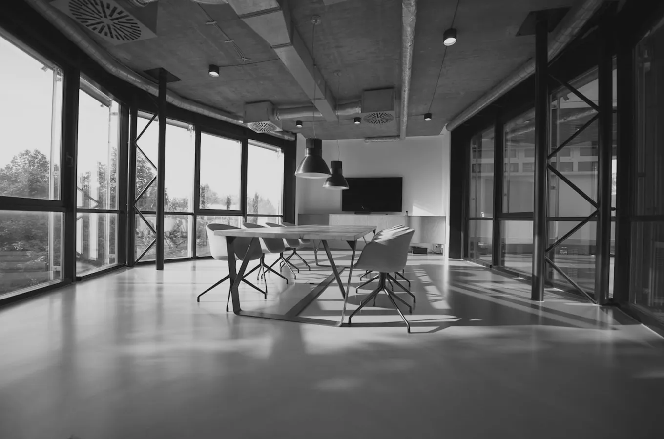 Modern conference room with large windows, a long table, swivel chairs, and hanging pendant lights.