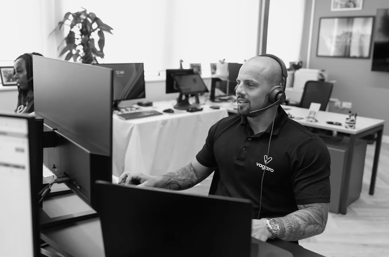 Man wearing headset and Vagaro polo shirt working at a desk with multiple monitors in an office.