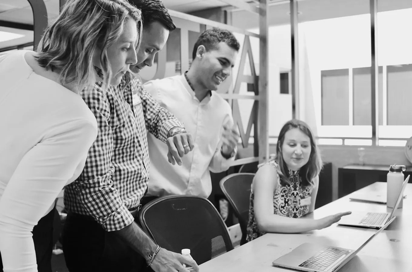 Four colleagues gathered around a table, focused on laptops during a collaborative work session in an office.