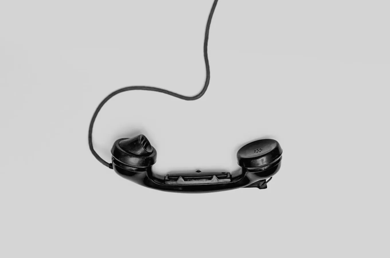 Black retro telephone handset with cord on a plain gray background.