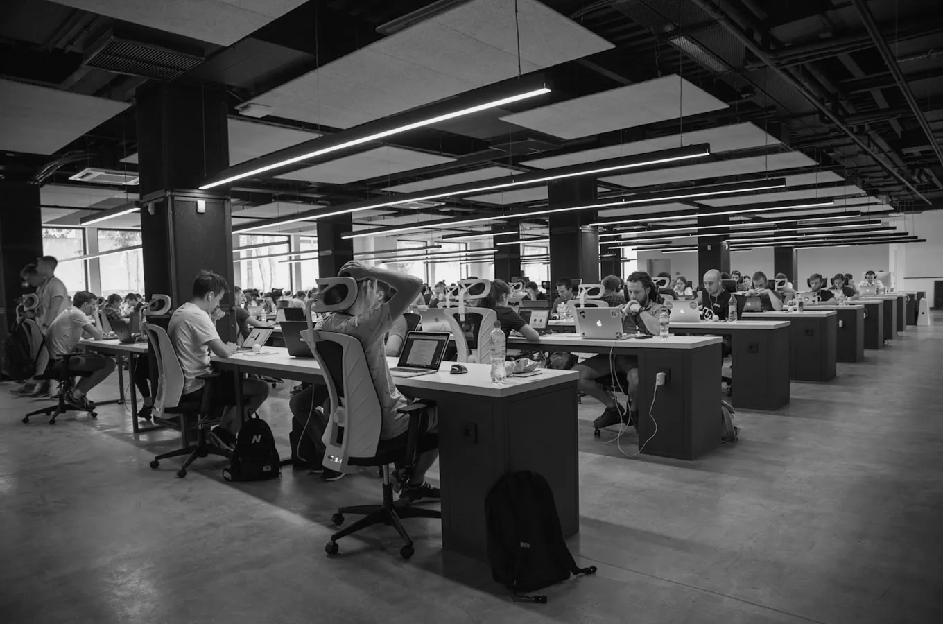 Large open office space with rows of people working on laptops at long desks.