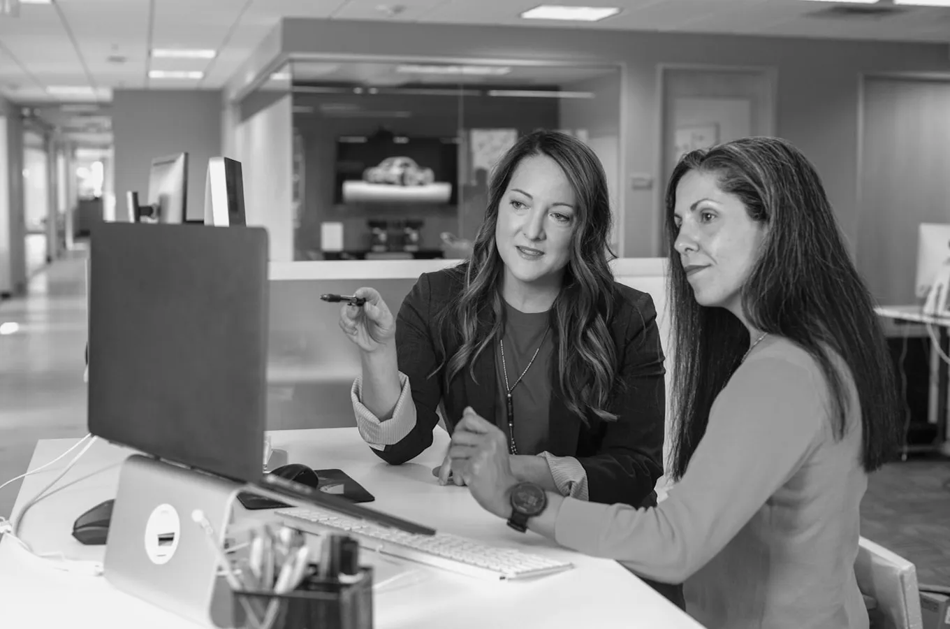Two women collaborating and discussing work while looking at a computer screen in an office.