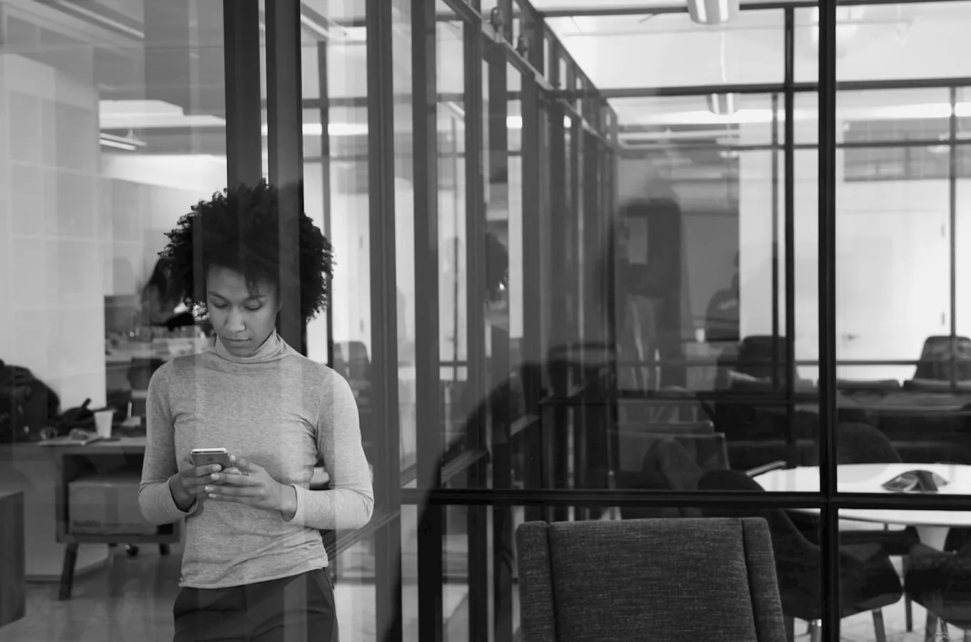 Woman with curly hair standing inside an office using a smartphone.