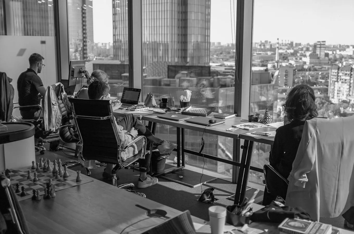 Four people working at desks in a high-rise office with large windows overlooking a cityscape.