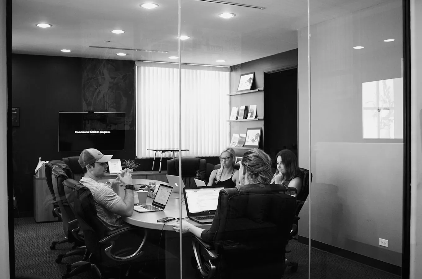 Four people having a meeting around a conference table with laptops in a modern office room.