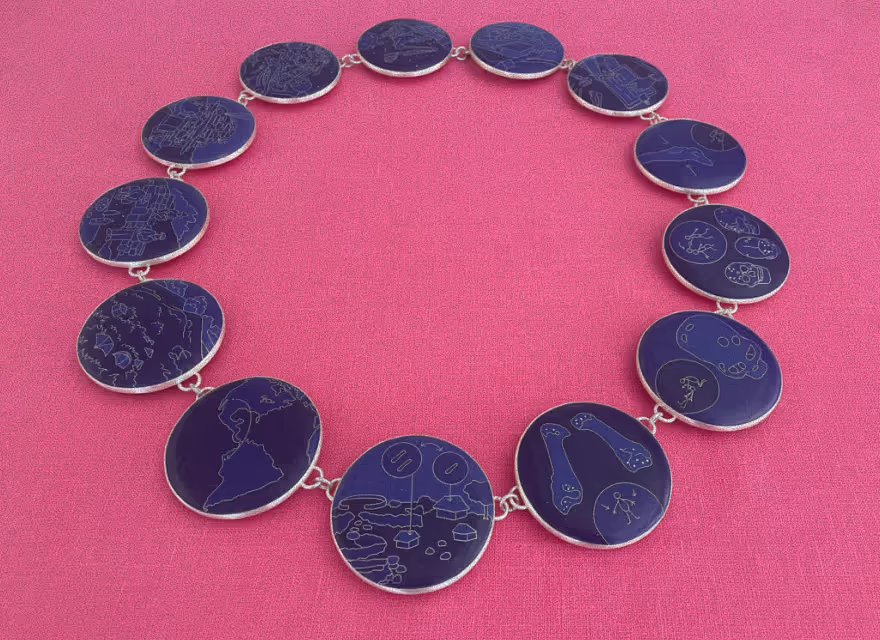 Necklace with round dark blue pendants engraved with various intricate line drawings of maps, bones, skulls, and diagrams, displayed on a pink fabric background.