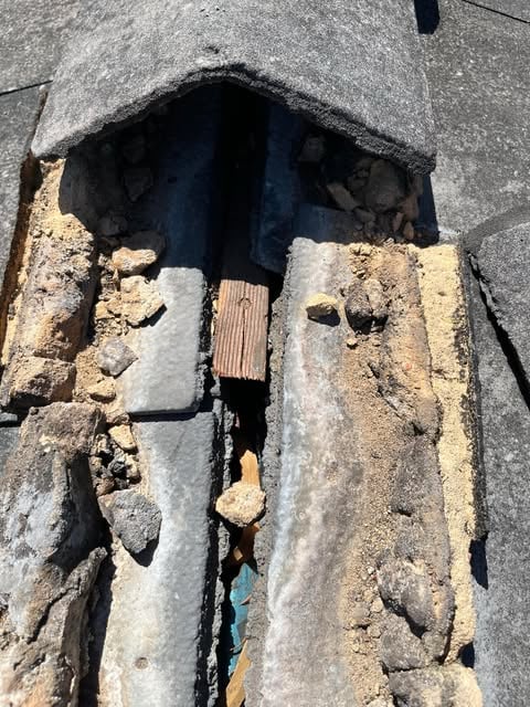 Close-up of a damaged roof showing torn roofing felt, exposed wooden plank, and accumulated debris.