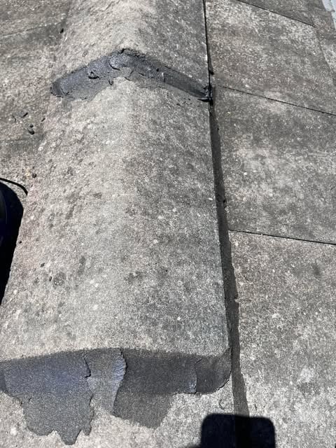 Close-up of a worn and cracked concrete roof ridge cap on a tiled roof under sunlight.