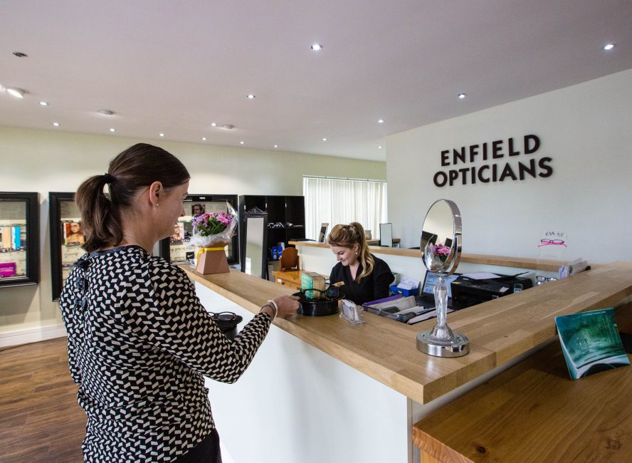 Customer at reception desk of Enfield Opticians, staff member working