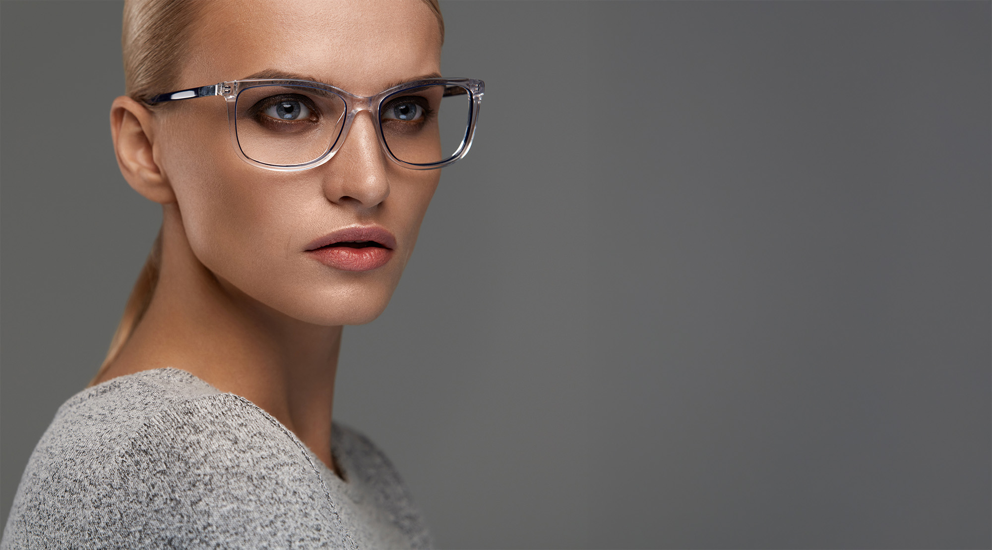 Stylish person wearing transparent glasses, looking to the side against gray background