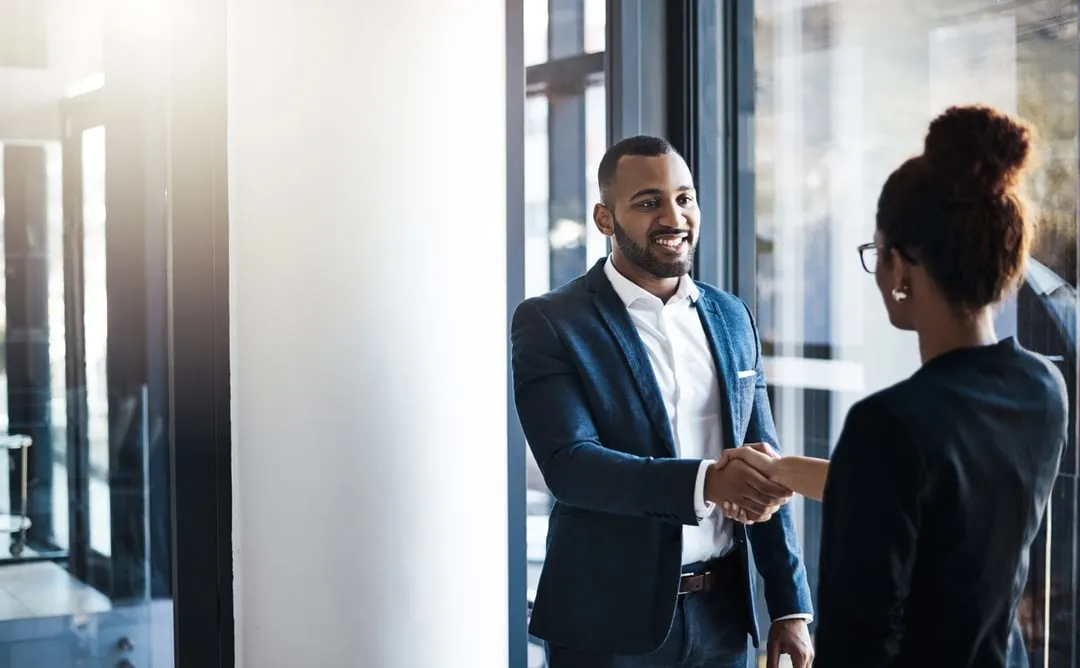 Two professionally dressed individuals shaking hands in a modern office environment.