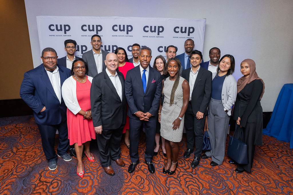 Group of professionally dressed diverse individuals posing in front of a backdrop with the word 'cup' and the slogan 'Inspire. Elevate. Empower.'