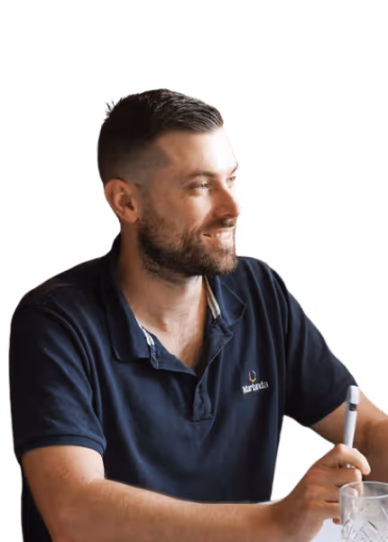 Bearded man with short hair wearing a navy Marlanda polo shirt, smiling and holding a pen.