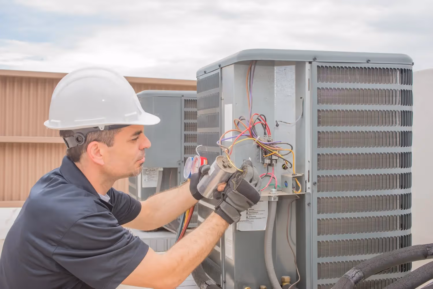 Technician in a hard hat inspecting components of a large commercial rooftop AC unit.