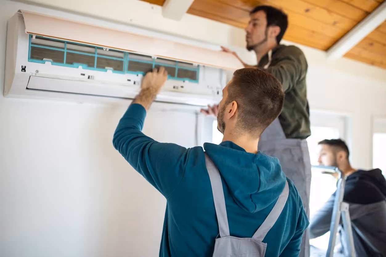 A team of two technicians is installing a wall-mounted air conditioner in a room.