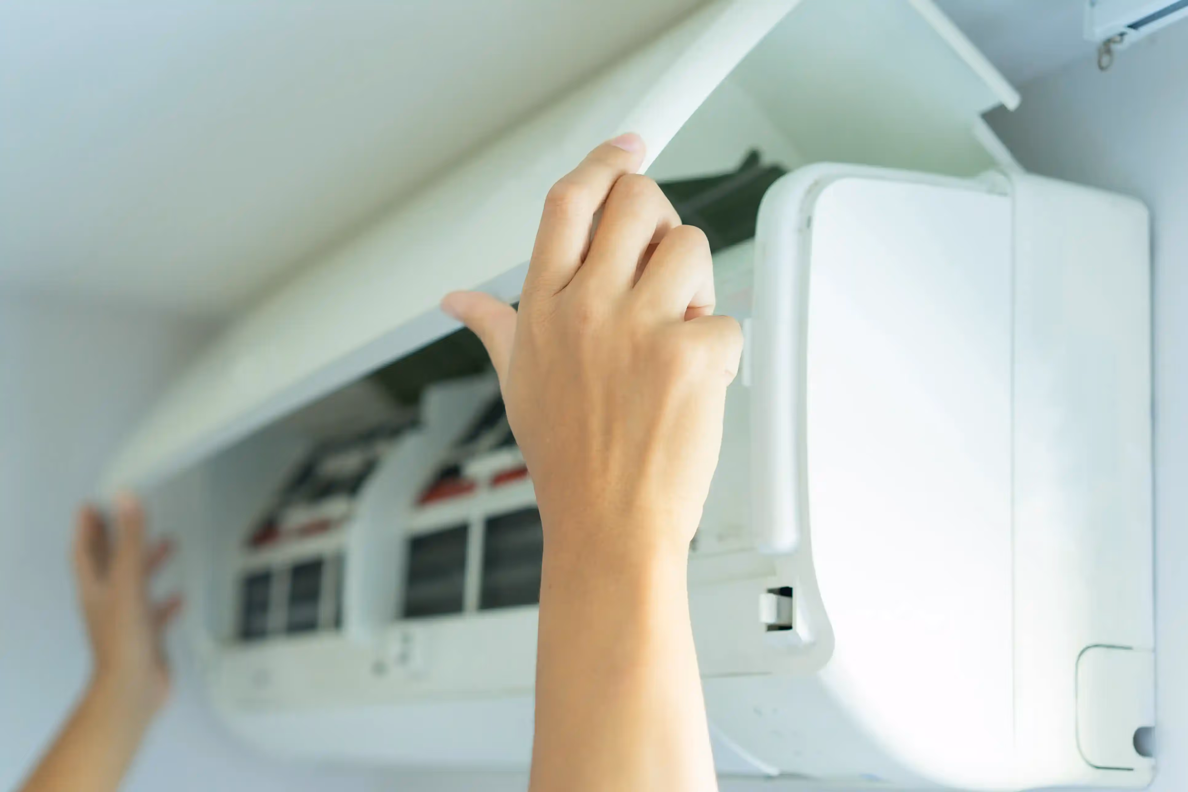 A close-up of a person's hands opening the cover of a wall-mounted air conditioner.
