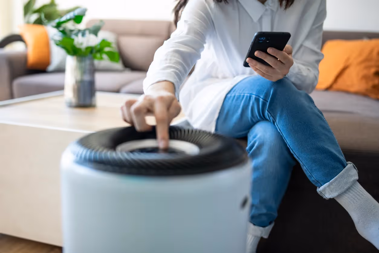 A person sits on a sofa looking at their phone next to an air purifier
